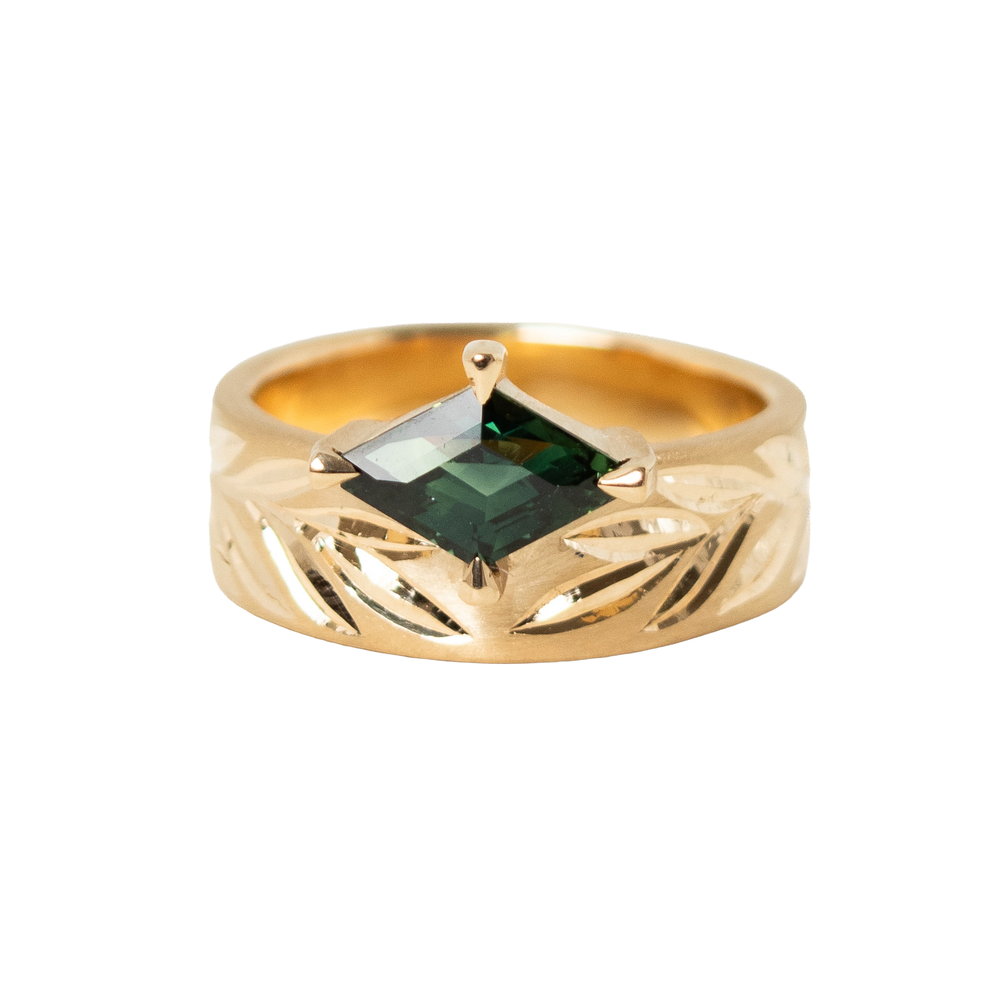 A 14k gold ring featuring a hexagon dark green sapphire in a prong eagle setting, with an hand engraved leaf pattern on the band, shown against a plain white background.