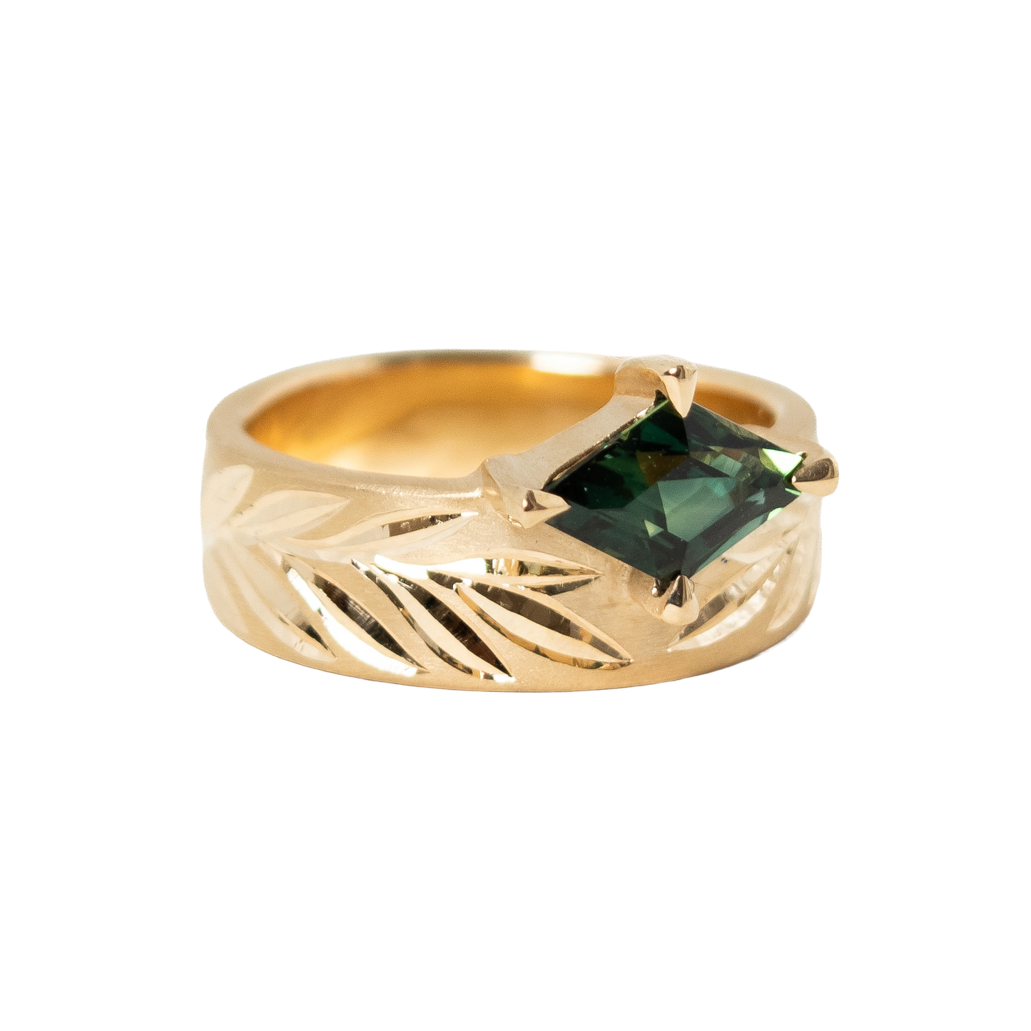 A 14k gold ring featuring a hexagon dark green sapphire in a prong eagle setting, with an hand engraved leaf pattern on the band, shown against a plain white background.