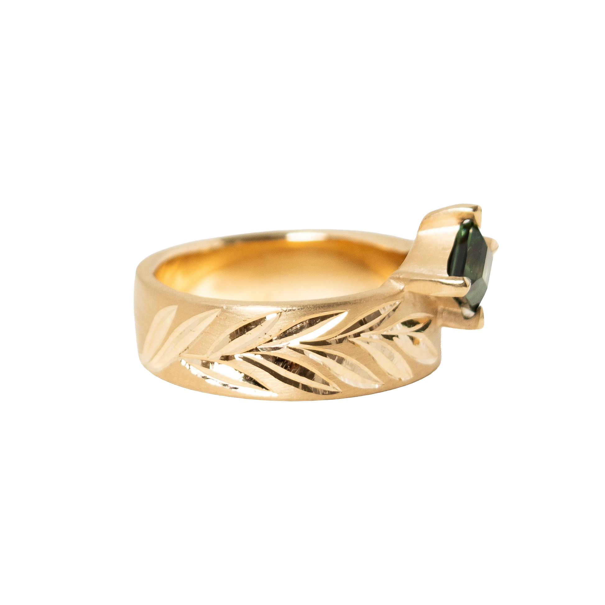 A 14k gold ring featuring a hexagon dark green sapphire in a prong eagle setting, with an hand engraved leaf pattern on the band, shown against a plain white background.