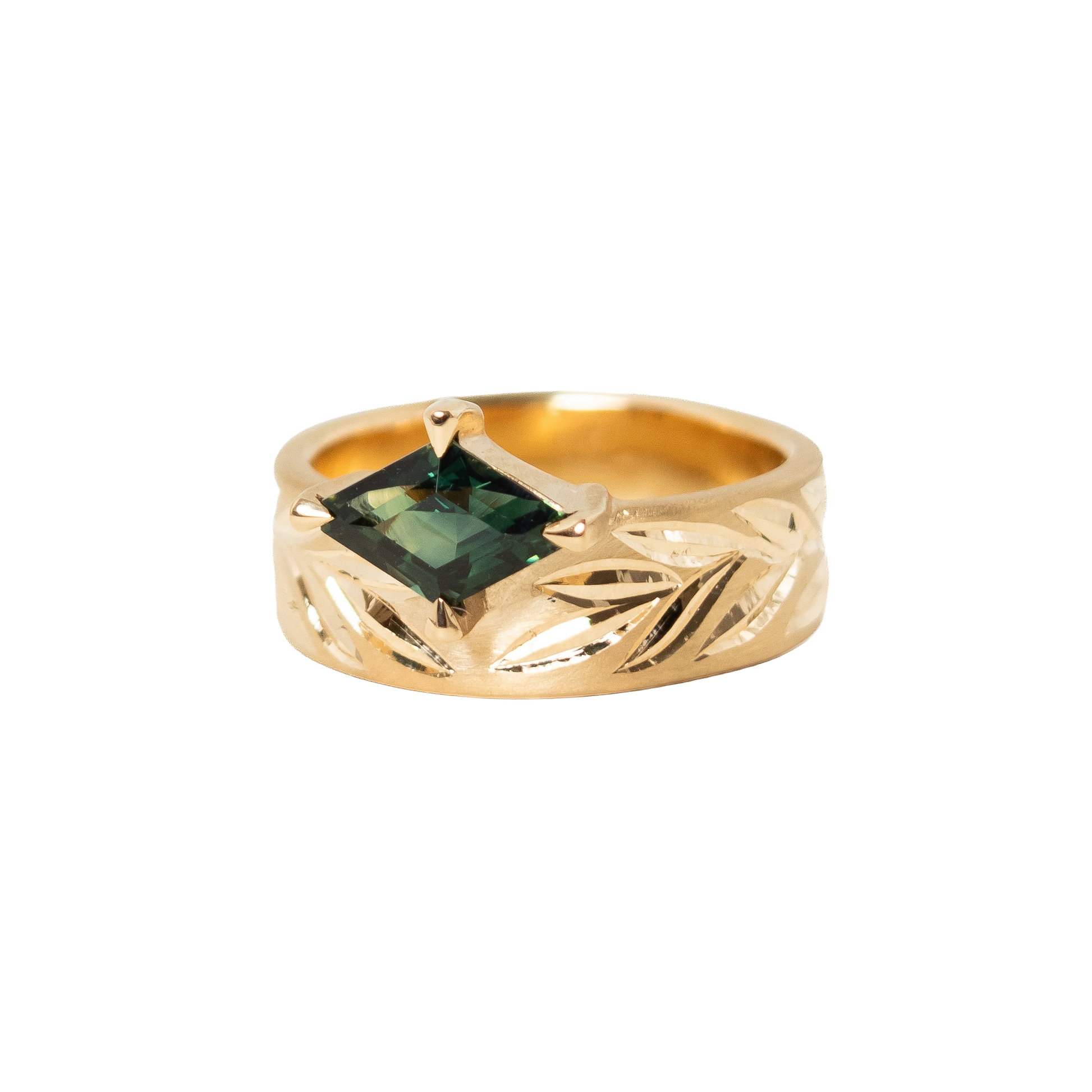 A 14k gold ring featuring a hexagon dark green sapphire in a prong eagle setting, with an hand engraved leaf pattern on the band, shown against a plain white background.