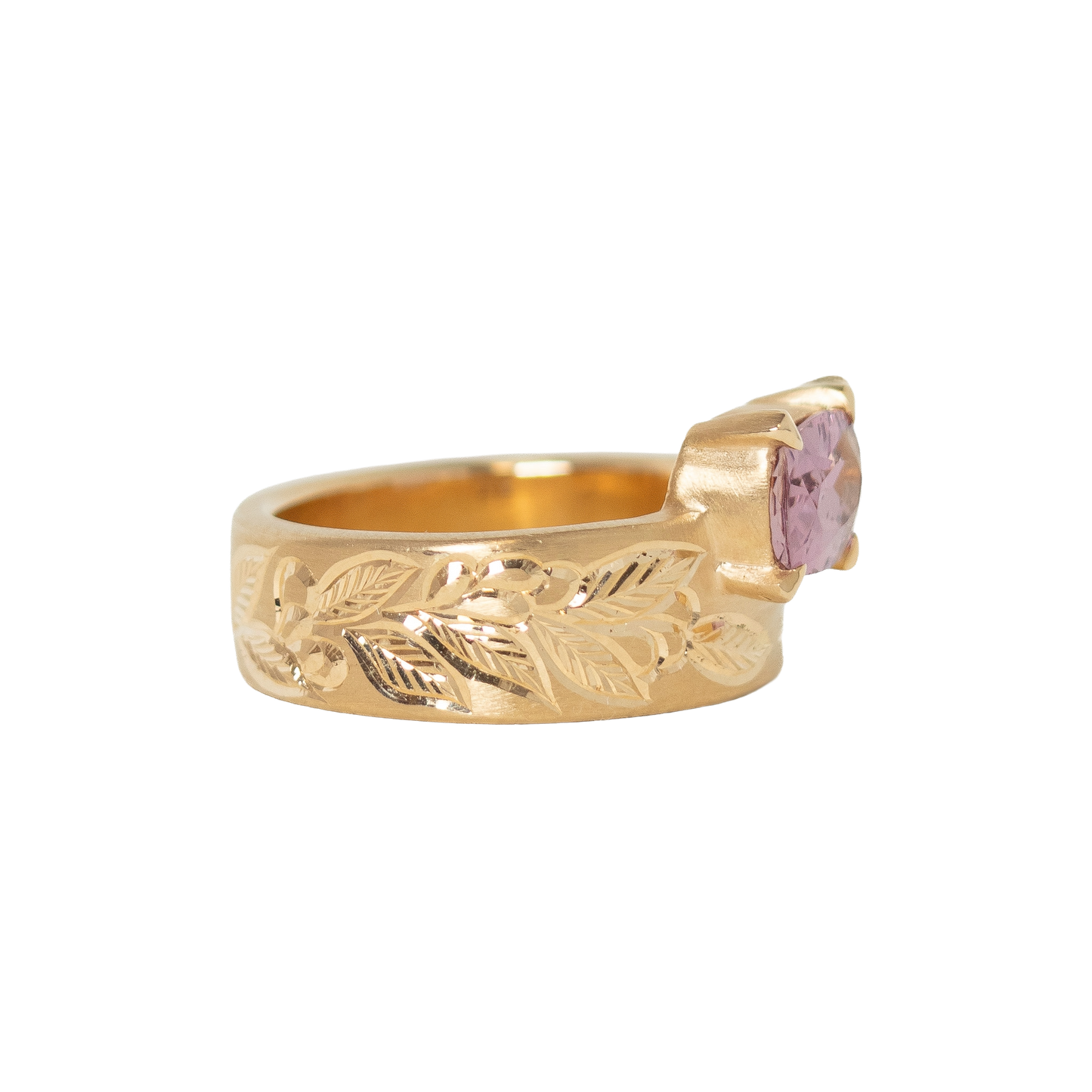 A 14k yellow gold ring featuring a cushion-cut pink sapphire in a prong setting, with an hand engraved leaf pattern on the band, shown against a plain white background.